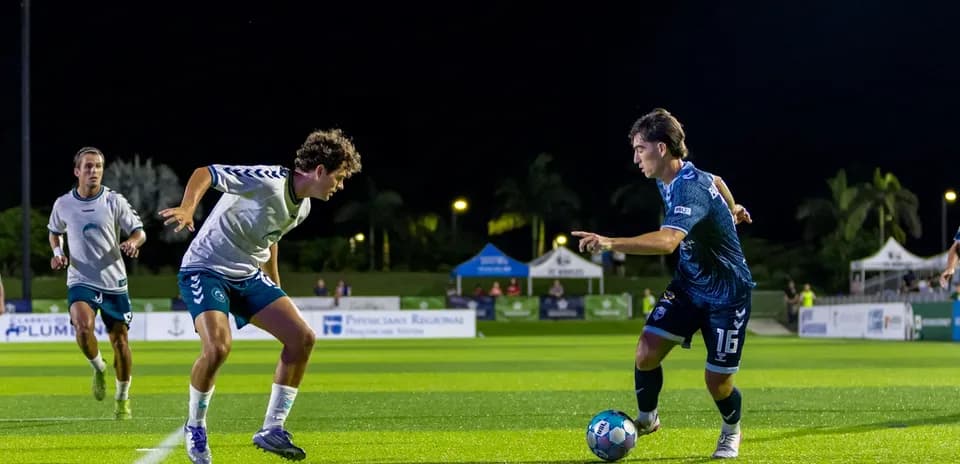 Jugador de fútbol driblando en partido nocturno