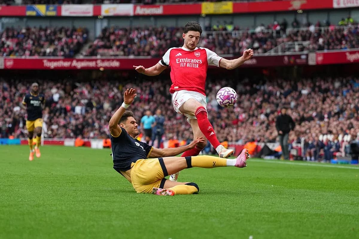 Jugador de Arsenal saltando sobre oponente caído