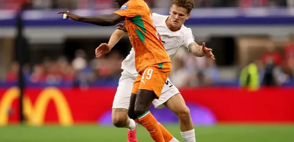Jugador con camiseta naranja driblando mientras es marcado