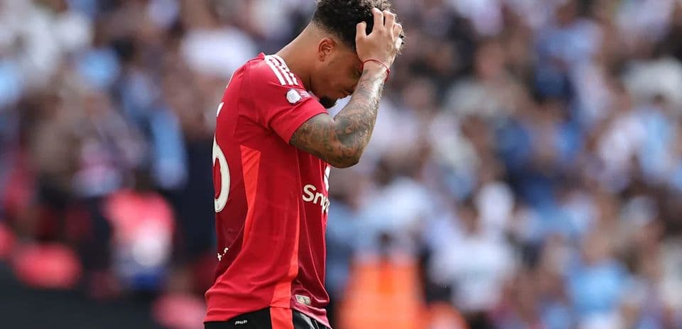 Jugador de fútbol con camiseta roja, cabizbajo en el campo